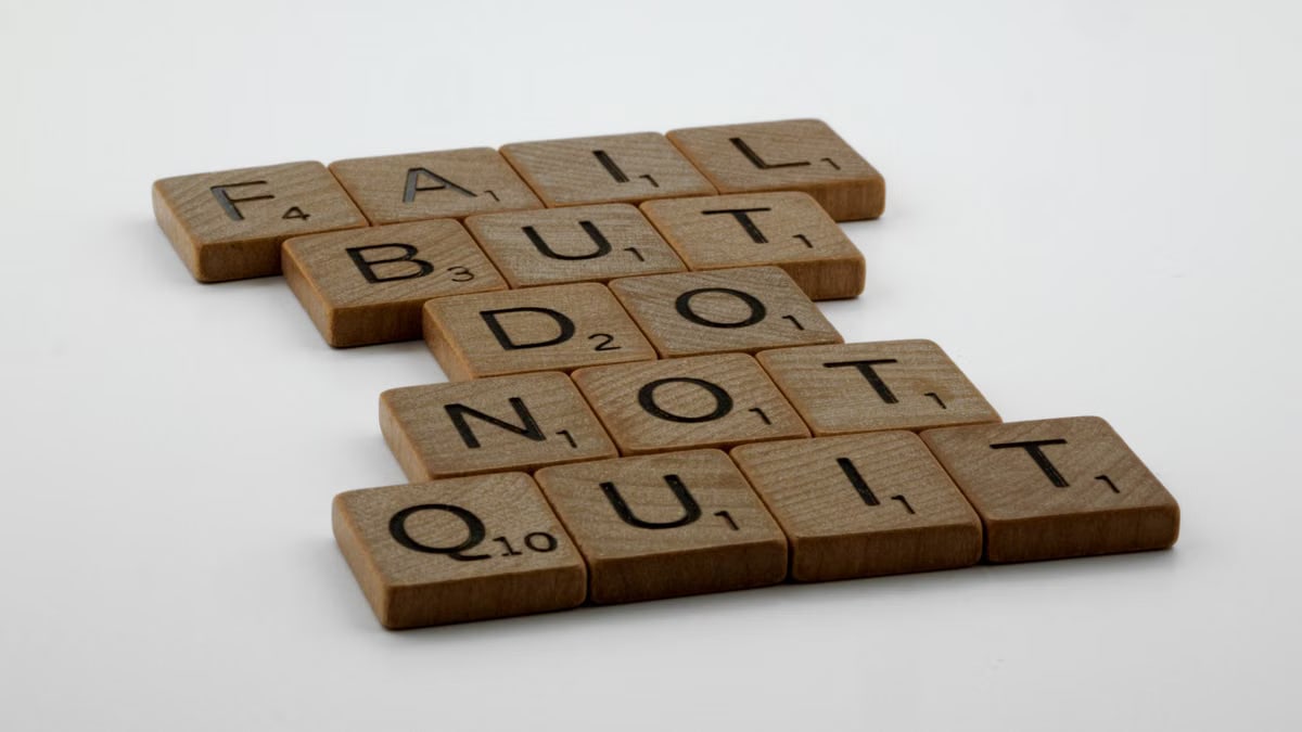 Wooden Scrabble tiles arranged to spell 'Fail but do not quit,' inspiring determination.